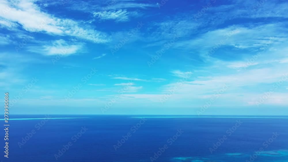A blue sky with some clouds above the Philippine Sea. Some turquoise spots are visible. Pan movement left, wide angle. A blue sky with some clouds above the Philippine Sea. Some turquoise spots are visible. Pan movement left, wide angle.
