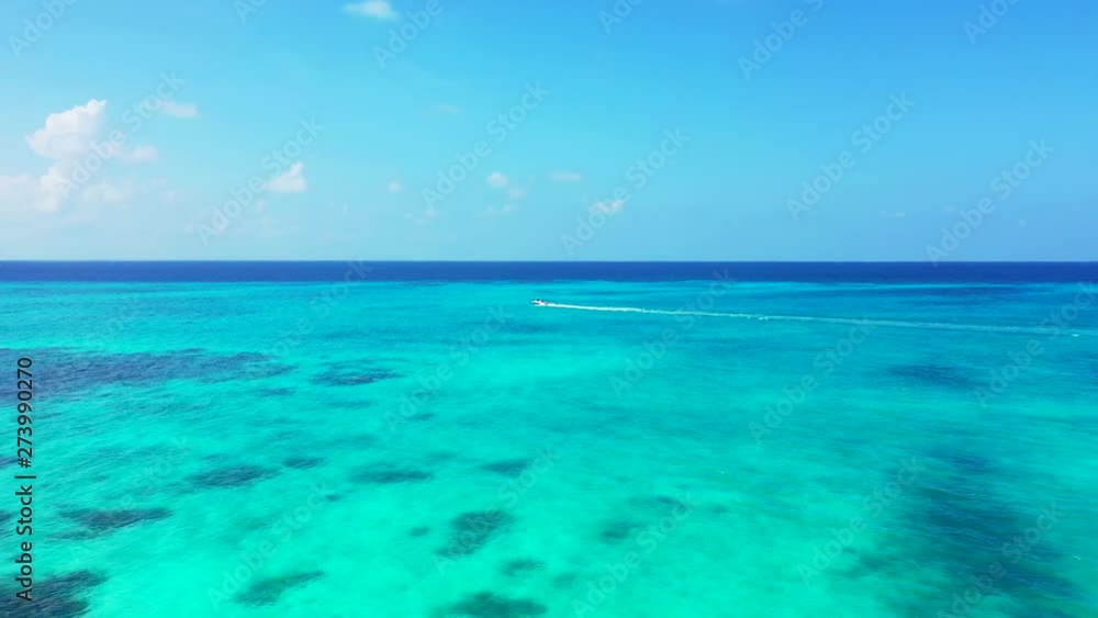 Aerial shot, following a white motorboat driving in turquoise blue water in the Caribbean. Dolly in with pan movements, wide angle Aerial shot, following a white motorboat driving in turquoise blue water in the Caribbean. Dolly in with pan movements, wide angle