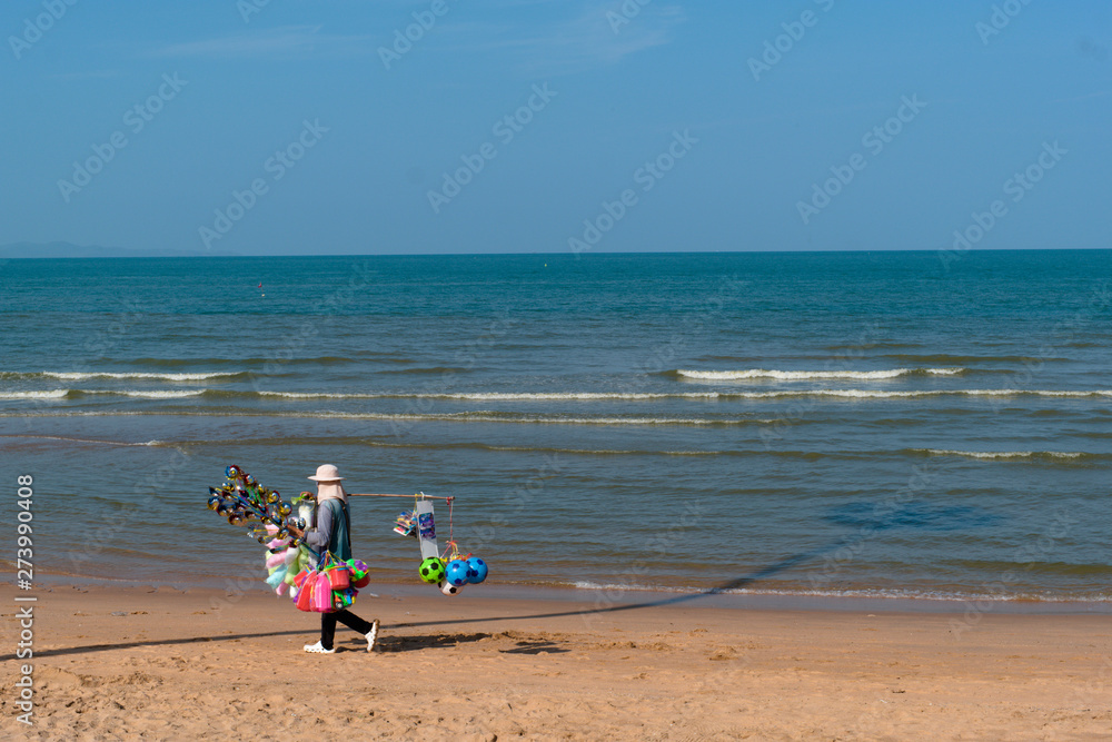 The seller walks at Pattaya beach to sell products such as baby toys, candy and balloons. The seller walks at Pattaya beach to sell products such as baby toys, candy and balloons.