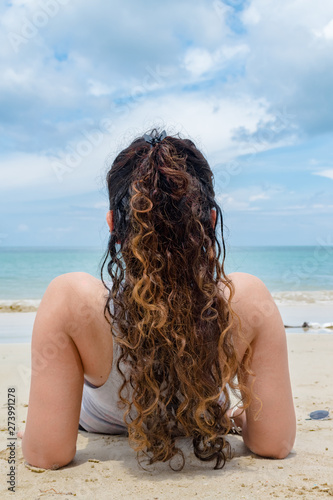 Amazing Back view of fair skinned Girl in mid 20s, having curly hairs of golden Color. She is relaxing & sunbathing solo on beach vacation, to exotic tropical island with clement weather & calm ocean. © Ashish_wassup6730