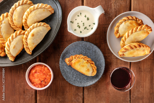 Empanadas with sauces and wine, shot from the top on a dark rustic wooden background