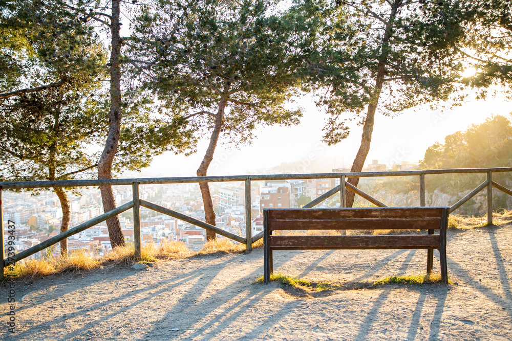Bench and trees with views at the city over Barcelona during sunset