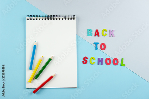 Top view of open notebook with colorful pencils and inscription by letters back to school on pastel blue and grey background. View from above, flat lay, copy space