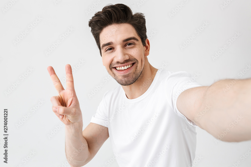 Excited happy young man posing isolated over white wall background make a selfie by camera. Excited happy young man posing isolated over white wall background make a selfie by camera.