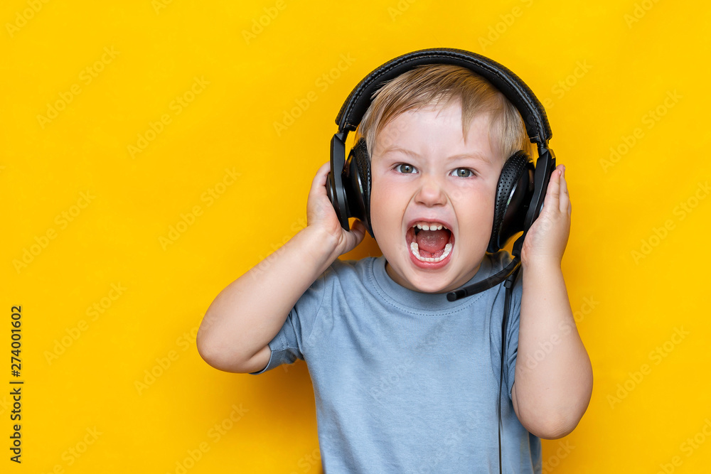 Little boy in modern headphones shouting, standing on yellow background Little boy in modern headphones shouting, standing on yellow background