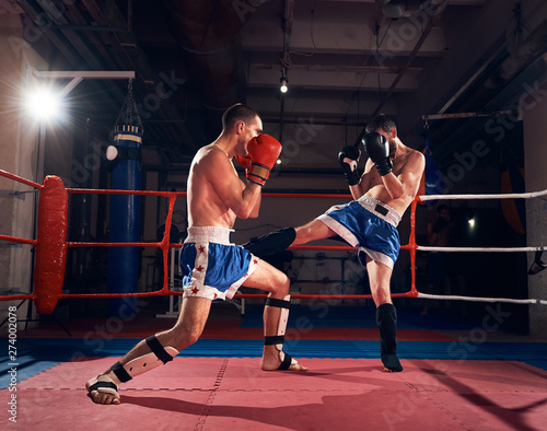 Two professional sportsmen boxers exercising kickboxing in the ring at the sport club photo
