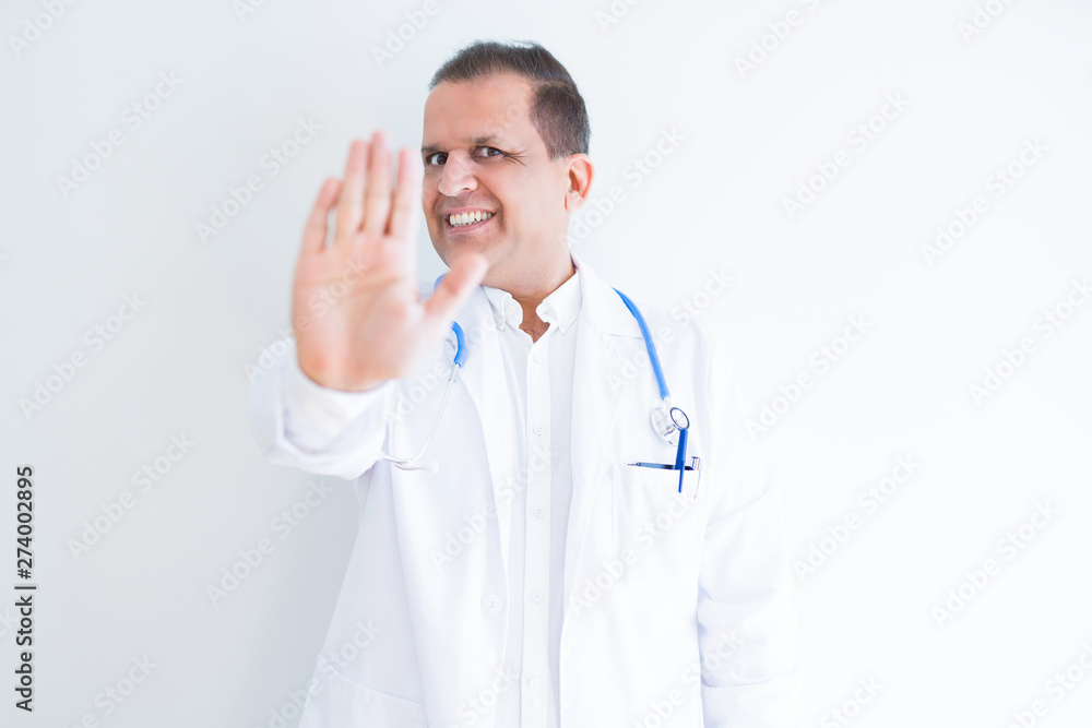Middle age doctor man wearing stethoscope and medical coat over white background doing stop sing with palm of the hand. Warning expression with negative and serious gesture on the face. Middle age doctor man wearing stethoscope and medical coat over white background doing stop sing with palm of the hand. Warning expression with negative and serious gesture on the face.