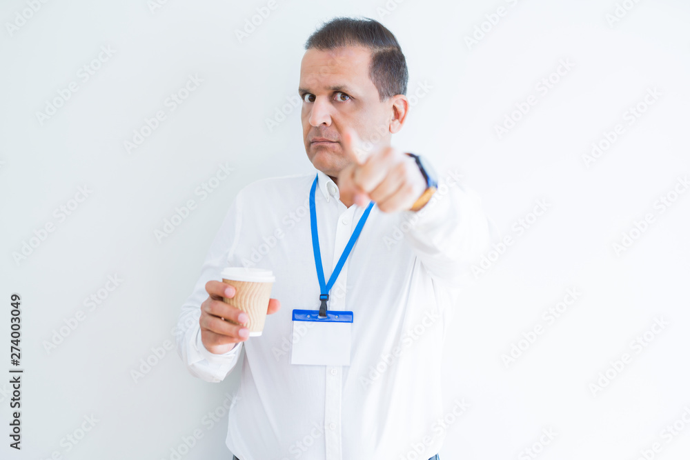 Middle age business man wearing ID card and drinking coffeeover white background pointing with finger to the camera and to you, hand sign, positive and confident gesture from the front