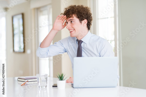 Young business man working with computer laptop at the office very happy and smiling looking far away with hand over head. Searching concept.