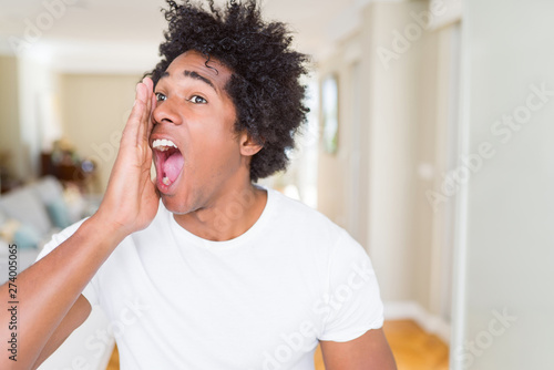 African American man at home shouting and screaming loud to side with hand on mouth. Communication concept.