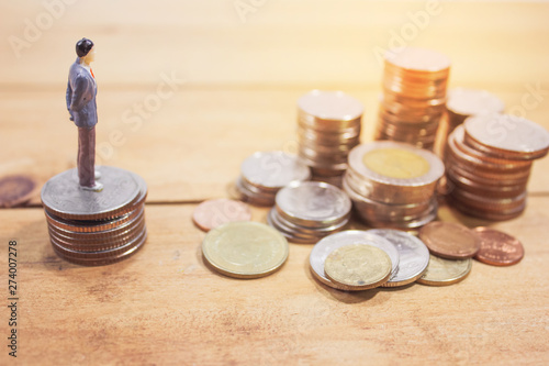 Miniature businessman stand on coins on wooden table. business planning concept.