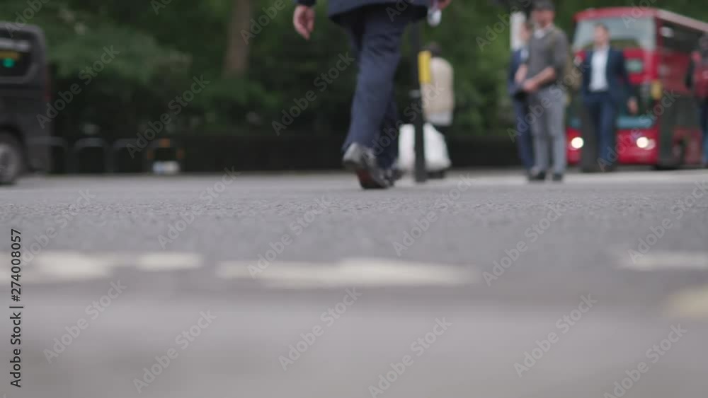 Businessman crosses busy street in London, smart navy blue suit trousers and shoes. Red London bus is visible in background