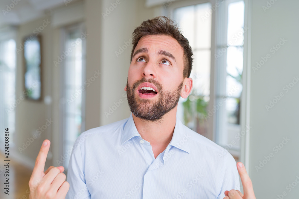 Handsome business man amazed and surprised looking up and pointing with fingers and raised arms. Handsome business man amazed and surprised looking up and pointing with fingers and raised arms.