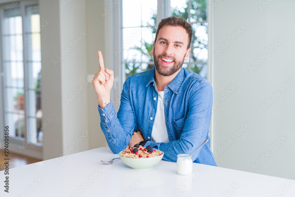 Handsome man eating cereals for breakfast at home with a big smile on face, pointing with hand and finger to the side looking at the camera. Handsome man eating cereals for breakfast at home with a big smile on face, pointing with hand and finger to the side looking at the camera.