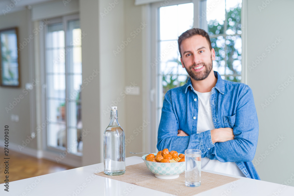 Handsome man eating pasta with meatballs and tomato sauce at home happy face smiling with crossed arms looking at the camera. Positive person. Handsome man eating pasta with meatballs and tomato sauce at home happy face smiling with crossed arms looking at the camera. Positive person.