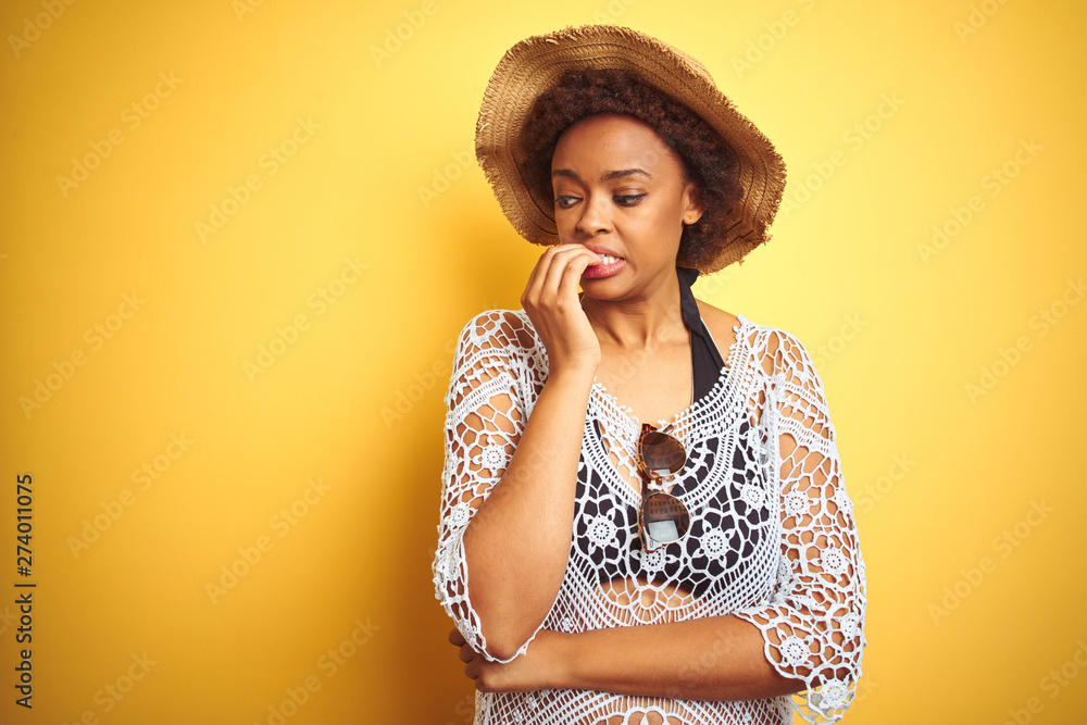 Young african american woman with afro hair wearing summer hat over white isolated background looking stressed and nervous with hands on mouth biting nails. Anxiety problem. Young african american woman with afro hair wearing summer hat over white isolated background looking stressed and nervous with hands on mouth biting nails. Anxiety problem.