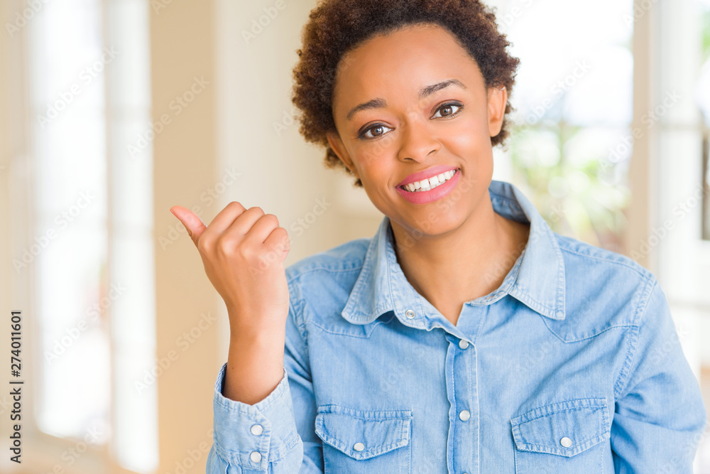 Young beautiful african american woman smiling with happy face looking and pointing to the side with thumb up. Young beautiful african american woman smiling with happy face looking and pointing to the side with thumb up.