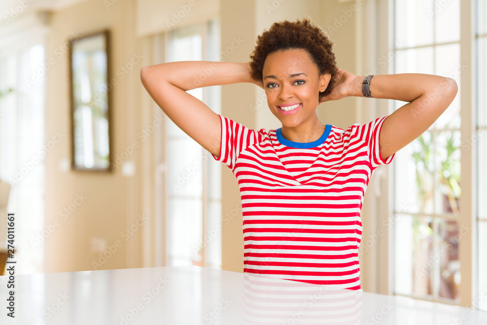 Young beautiful african american woman at home Relaxing and stretching with arms and hands behind head and neck, smiling happy Young beautiful african american woman at home Relaxing and stretching with arms and hands behind head and neck, smiling happy