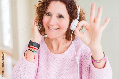 Senior woman wearing headphones listening to music doing ok sign with fingers  excellent symbol