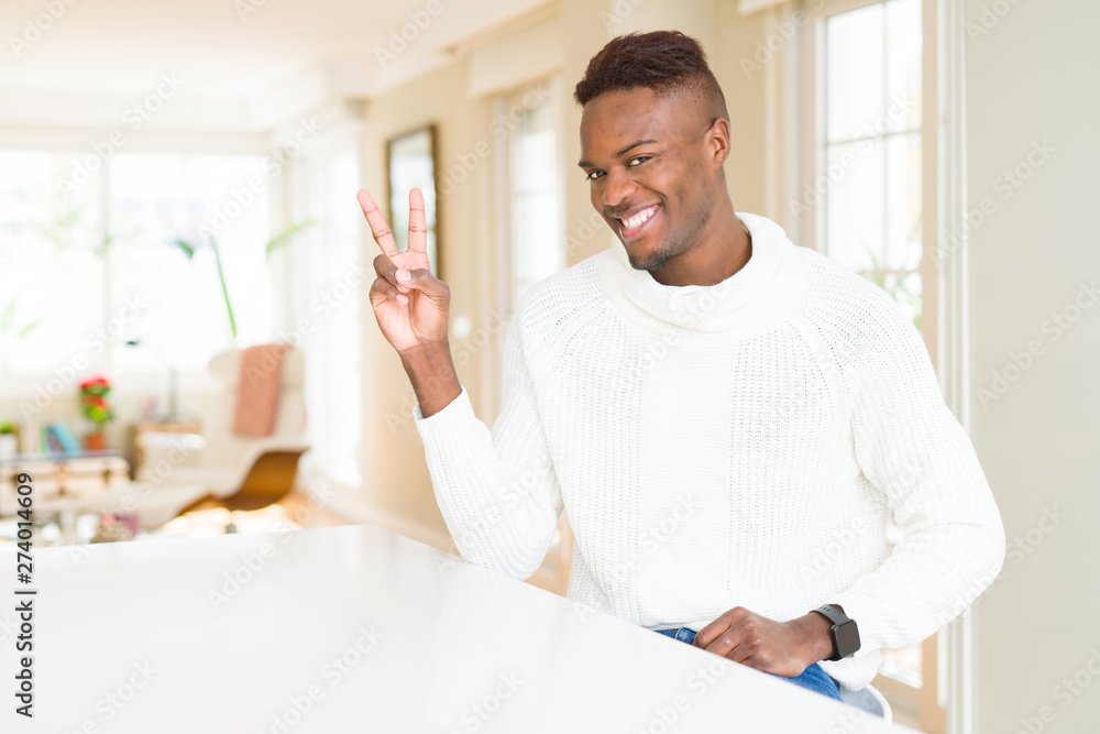 Handsome african american man on white table smiling with happy face winking at the camera doing victory sign. Number two.