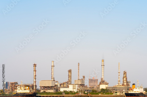 Crude oil refinery plant and many chimney with petrochemical tanker or cargo ship at coast of river on sky afternoon bright day at thailand with copy space