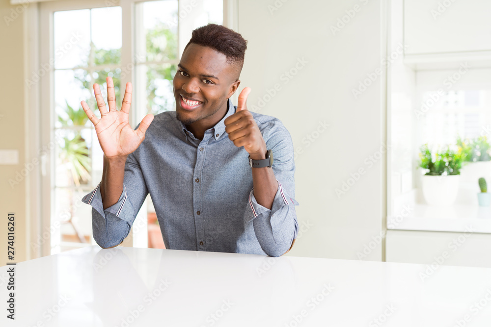 Handsome african american man on white table showing and pointing up with fingers number six while smiling confident and happy. Handsome african american man on white table showing and pointing up with fingers number six while smiling confident and happy.
