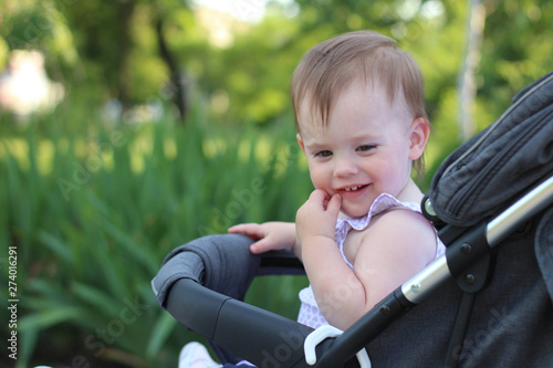 little, beautiful, smiling, cute redhead baby in a pram out-of-doors in a sleeveless shirt looking down