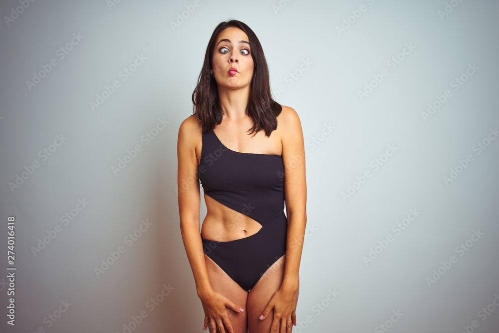 Beautiful woman wearing bikini swimwear over white isolated background making fish face with lips, crazy and comical gesture. Funny expression.