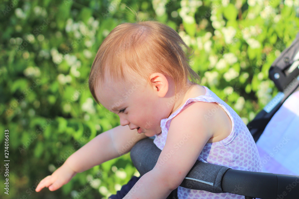 little, beautiful, smiling, cute redhead baby in a sleeveless shirt in a pram out-of-doors drops hands down and looking forward little, beautiful, smiling, cute redhead baby in a sleeveless shirt in a pram out-of-doors drops hands down and looking forward