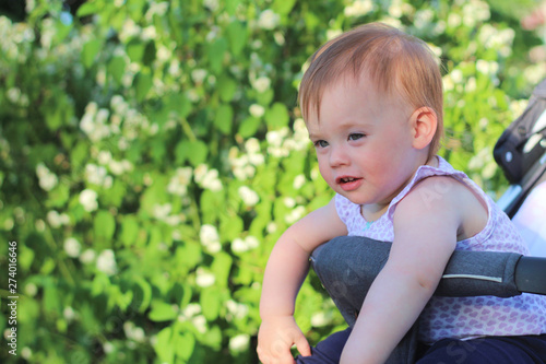 little, beautiful, smiling, cute redhead baby in a sleeveless shirt in a pram out-of-doors drops hands down and looking forward