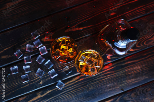 Two glasses of whiskey with ice cubes served on wooden planks.