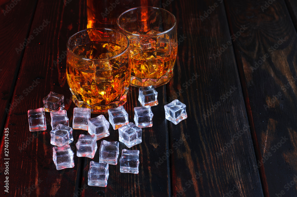 Two glasses of whiskey with ice cubes served on wooden planks. Two glasses of whiskey with ice cubes served on wooden planks.