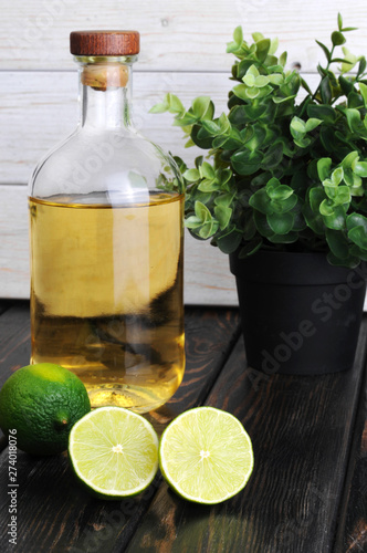Tequila bottle with fresh lime on a wooden table.Gold Mexican tequila with lime and salt.