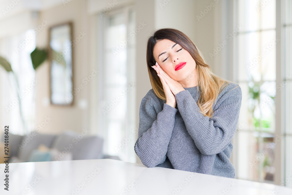 Young beautiful woman wearing winter sweater at home sleeping tired dreaming and posing with hands together while smiling with closed eyes. Young beautiful woman wearing winter sweater at home sleeping tired dreaming and posing with hands together while smiling with closed eyes.