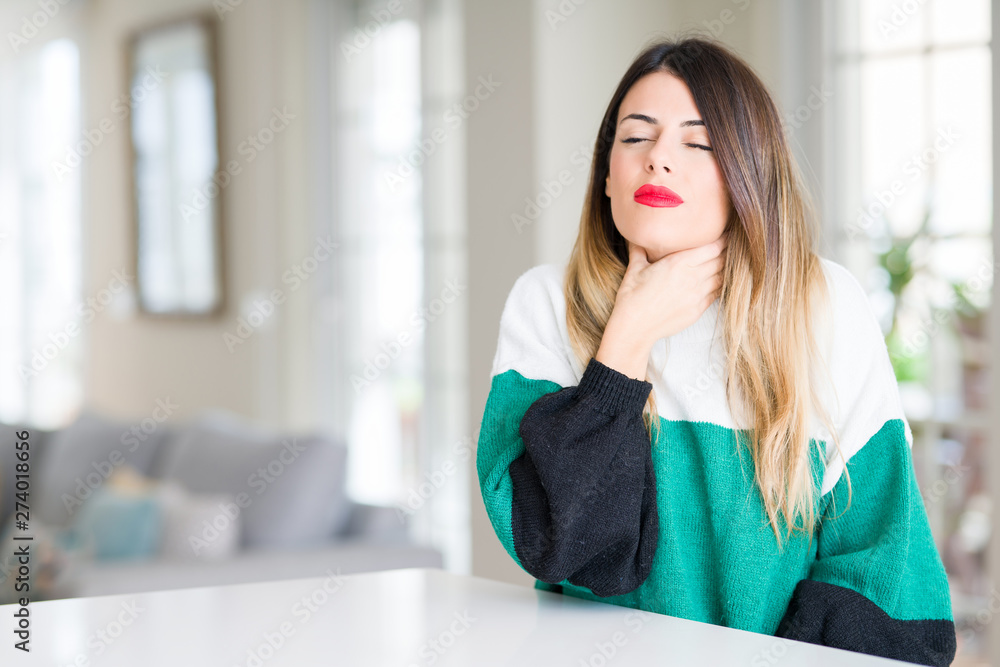 Young beautiful woman wearing winter sweater at home Touching painful neck, sore throat for flu, clod and infection Young beautiful woman wearing winter sweater at home Touching painful neck, sore throat for flu, clod and infection