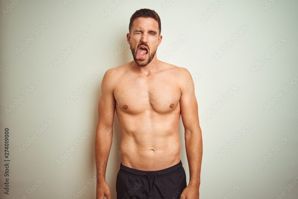 Young handsome shirtless man over isolated background sticking tongue out happy with funny expression. Emotion concept.
