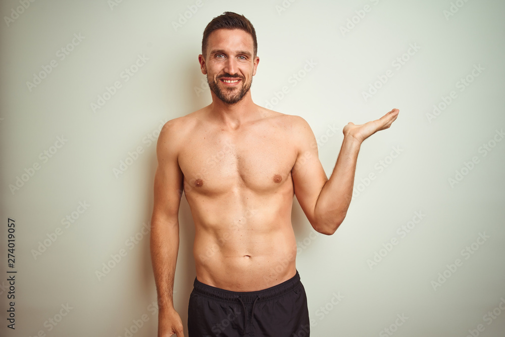Young handsome shirtless man over isolated background smiling cheerful presenting and pointing with palm of hand looking at the camera.