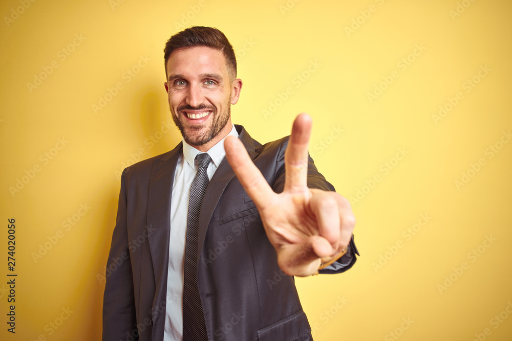 Young handsome business man over yellow isolated background smiling looking to the camera showing fingers doing victory sign. Number two. Young handsome business man over yellow isolated background smiling looking to the camera showing fingers doing victory sign. Number two.