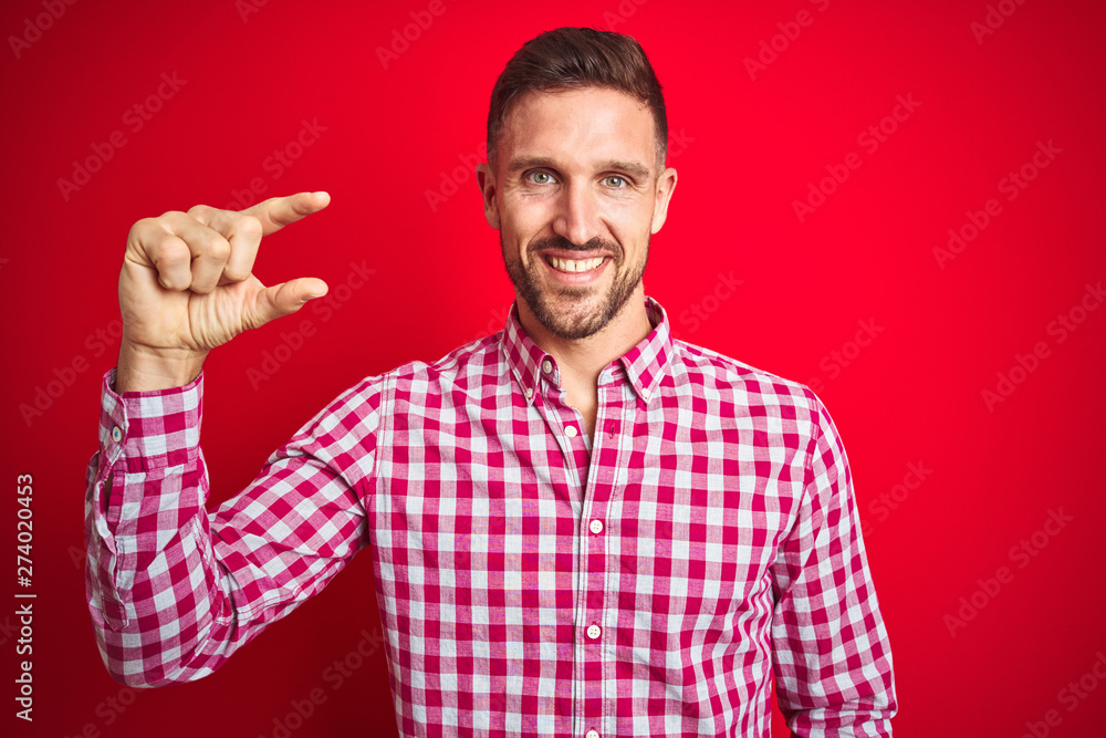 Young handsome man over red isolated background smiling and confident gesturing with hand doing small size sign with fingers looking and the camera. Measure concept. Young handsome man over red isolated background smiling and confident gesturing with hand doing small size sign with fingers looking and the camera. Measure concept.