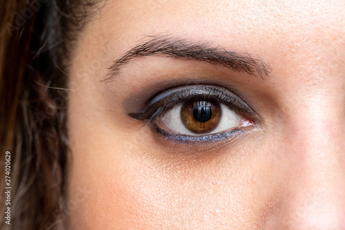 A close-up view on the open eye of a beautiful Caucasian woman with brown iris and smoky blue eyeshadow. Macro view of eye makeup and healthy skin under the eyes.