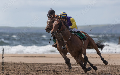 Two race jockeys battling for first place, horse racing action on the beach