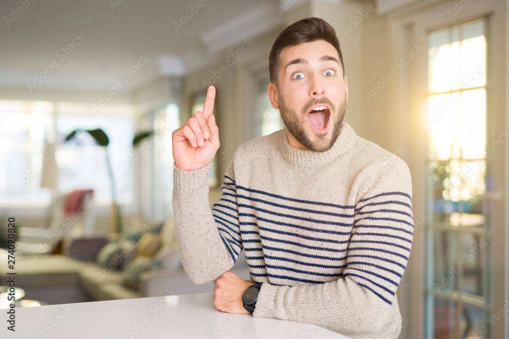 Young handsome man at home pointing finger up with successful idea. Exited and happy. Number one. Young handsome man at home pointing finger up with successful idea. Exited and happy. Number one.