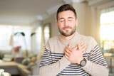 Young handsome man at home smiling with hands on chest with closed eyes and grateful gesture on face. Health concept.