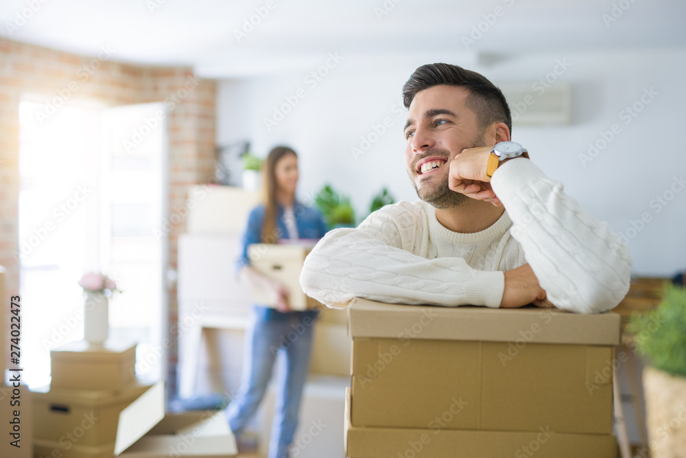 Young couple moving to a new home, handsome man smiling leaning on cardboard boxes Young couple moving to a new home, handsome man smiling leaning on cardboard boxes