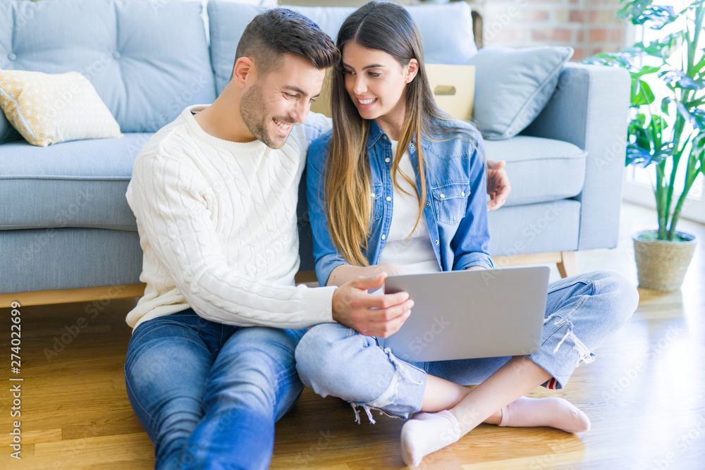 Young couple sitting on the floor of new home using computer laptop and smiling happy for moving to a new home Young couple sitting on the floor of new home using computer laptop and smiling happy for moving to a new home