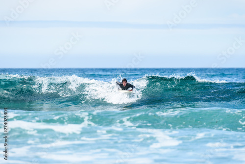 Surfer man with surfboard is paddling on the wave.