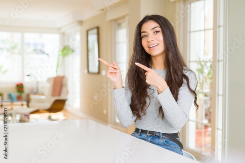 Young beautiful woman at home smiling and looking at the camera pointing with two hands and fingers to the side.