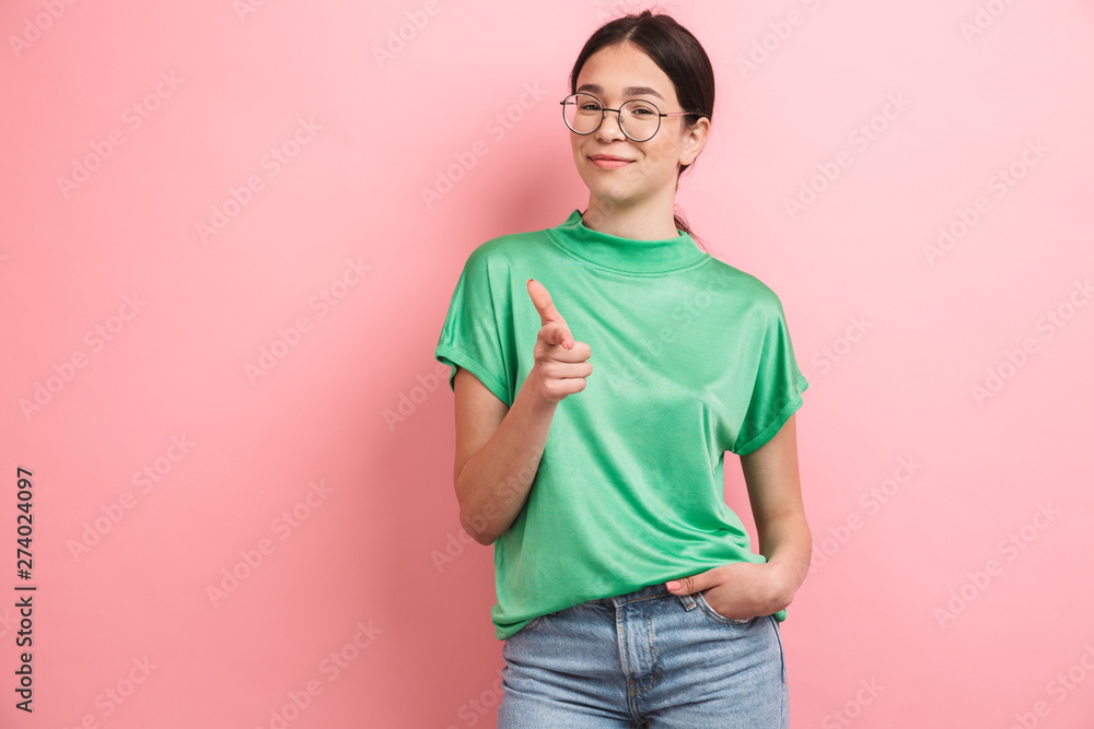 Photo of joyous young girl wearing round eyeglasses smiling and pointing finger at camera Photo of joyous young girl wearing round eyeglasses smiling and pointing finger at camera