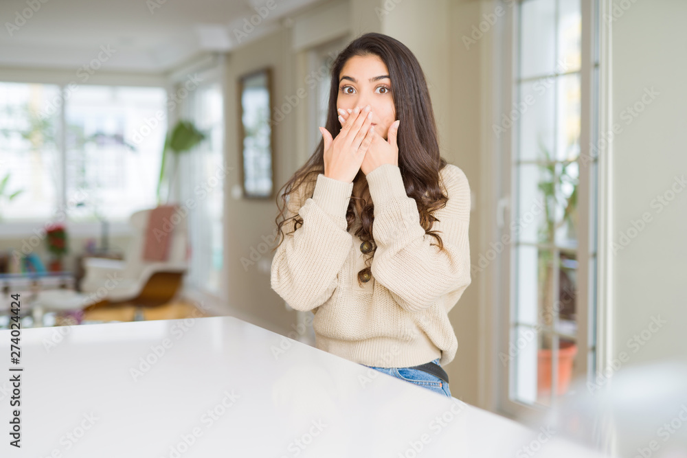 Young beautiful woman at home shocked covering mouth with hands for mistake. Secret concept.