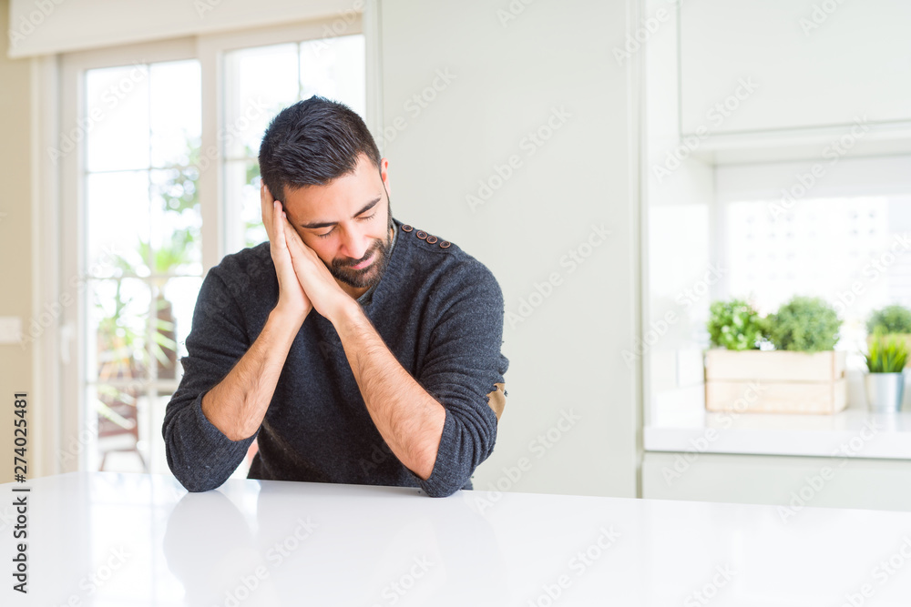 Handsome hispanic man wearing casual sweater at home sleeping tired dreaming and posing with hands together while smiling with closed eyes. Handsome hispanic man wearing casual sweater at home sleeping tired dreaming and posing with hands together while smiling with closed eyes.